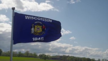 Rüzgarda dalgalanan bayrak direğinde Wisconsin bayrağı, mavi gökyüzü arka planı.