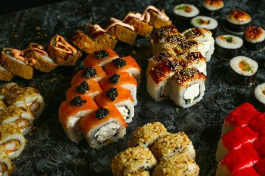 Siyah bir arka planda yansımalı geleneksel lezzetli suşi rulosu. Pilavlı suşi, kırmızı balık, somon balığı. Suşi menüsü. Japon mutfağı, restoran. Deniz ürünleri, Asya yemekleri.
