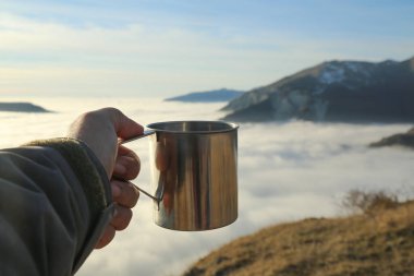 Gezgin adam bulutlu dağlarda bir fincan çayla oturuyor. Bakış açısı