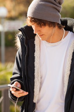 Genç yakışıklı adam açık havada telefona danışıyor.