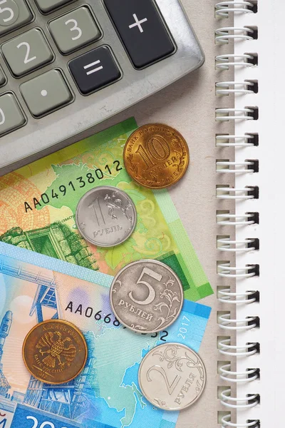 Hesap makinesinden, Rus parasından ve defterden bir kompozisyon. Banknotlar ve madeni paralar. Muhasebe ya da aile bütçesi hakkında dikey çizim. Gelir ve giderlerin hesaplanması. Yukarıdan görüntüle