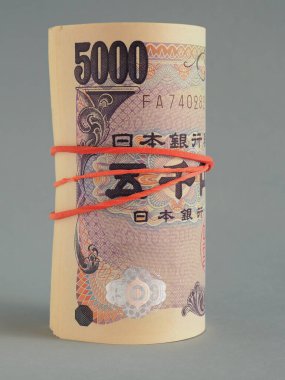 Yakın planda 5,000 yenlik Japon banknotları var. Koyu gri arka plan. Banknotlar paketlenmiş ve elastik bir bantla bağlanmış. Dikey çizim. Depozito ya da kredi. Makro