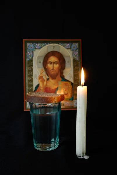 Burning candle, icon, a glass with water and breads — Stock Photo, Image