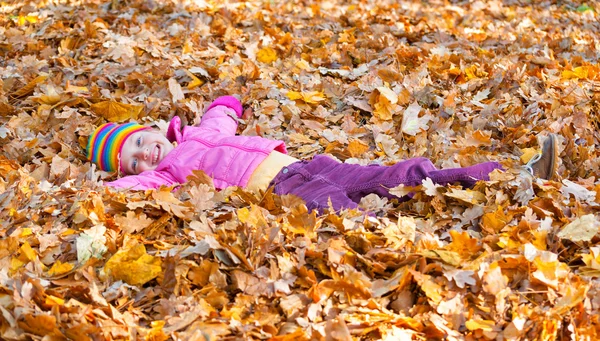 Meisje ligt op gele bladeren in de herfst park — Stockfoto