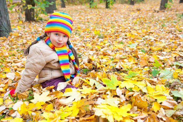 Niña sentarse en hojas amarillas en el parque de otoño — Foto de Stock