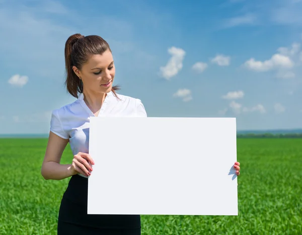 Girl with blank billboard on green field — Stock Photo, Image