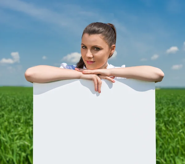 Girl with blank billboard on green field — Stock Photo, Image