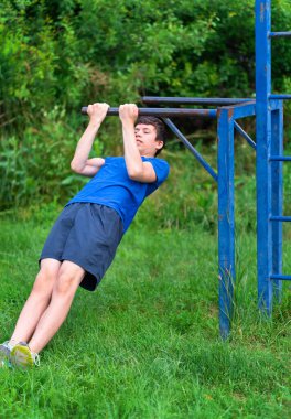 Dışarıda spor yapan genç bir çocuk, bahçede spor yapıyor, yatay bara doğru çekiliyor, sağlıklı bir yaşam tarzı var.