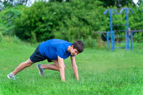 Genç çocuk dışarıda spor yapıyor, bahçede spor yapıyor, çömeliyor ve ısınıyor, sağlıklı bir yaşam sürüyor.