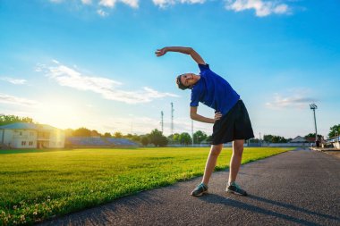 Genç çocuk stadyum pistinde fiziksel egzersiz yapıyor. Yeşil çimenli bir futbol sahası. Spor ve sağlık konsepti.