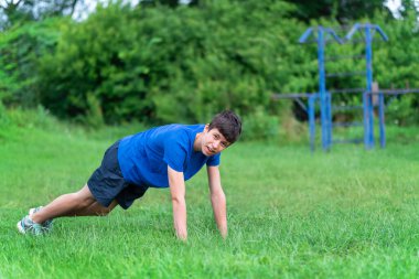 Genç çocuk dışarıda spor yapıyor, bahçede spor yapıyor, çömeliyor ve ısınıyor, sağlıklı bir yaşam sürüyor.