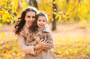 Sonbahar parkında bir anne ve kızın portresi. Mutlu insanlar güzel sarı ağaçların arkasında poz verirler. Sarılırlar ve birlikte mutlu olurlar..