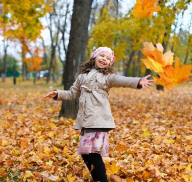 Sarı yapraklarla oynayan kız. Sonbahar parkındaki mutlu bir çocuğun portresi..