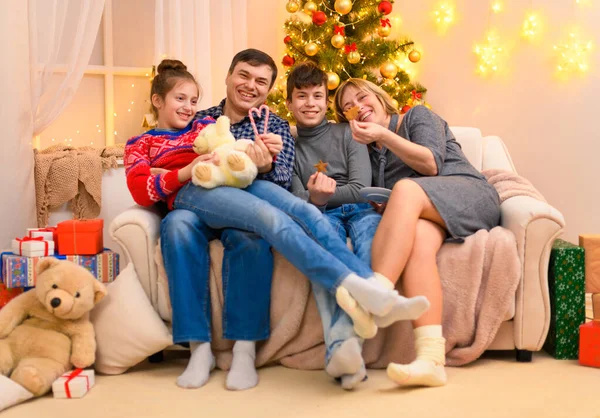 寒假的概念 一家人坐在沙发上 摆姿势庆祝新年或圣诞节 孩子和父母 节日彩灯和礼物 圣诞树装饰玩具 — 图库照片