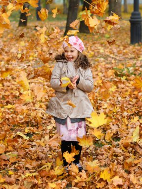 Sarı yapraklarla oynayan kız. Sonbahar parkındaki mutlu bir çocuğun portresi..