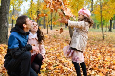 Bir sonbahar parkında aile fotoğrafı. Sarı yapraklarla oynayan mutlu insanlar..