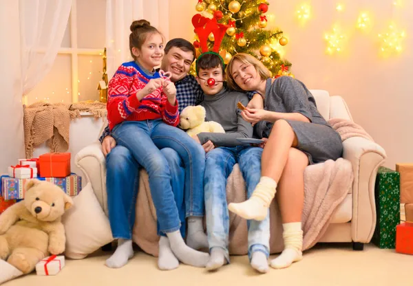 寒假的概念 一家人坐在沙发上 室内有新年或圣诞节的装饰 孩子和父母 节日彩灯和礼物 圣诞树装饰玩具 — 图库照片