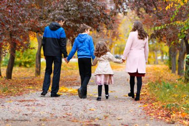 Aile, patika boyunca sonbahar parkında yürüyor. Çevreleri güzel doğa ve sarı ve kırmızı yapraklı ağaçlarla çevrili.