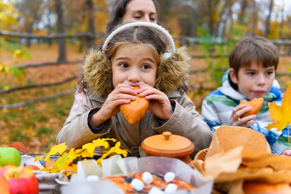 一个女孩吃面包的肖像 快乐的一家人在秋天的城市公园休息 人们坐在桌旁 一边吃饭一边说话 在美丽的黄树的衬托下 — 图库照片