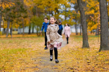 Çocuklar sonbahar parkında patika boyunca koşarlar. Oynuyorlar, gülüyorlar, çok eğleniyorlar. Güzel doğa ve sarı yapraklı ağaçlar..