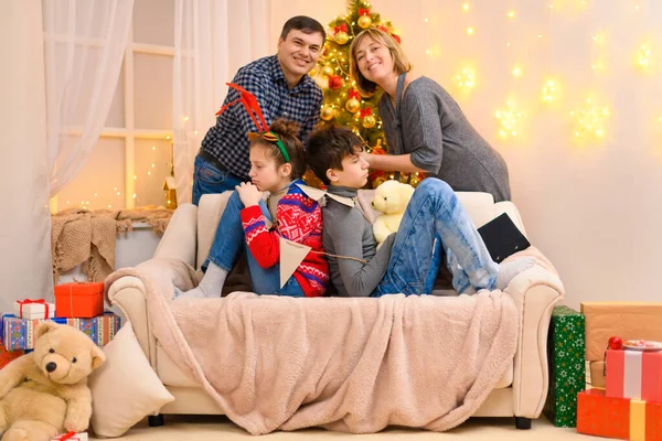 寒假的概念 家庭在室内摆设与新年或圣诞节装饰 孩子们坐在沙发上 绑着花环 父母们亲吻着 假日灯具和礼物 — 图库照片