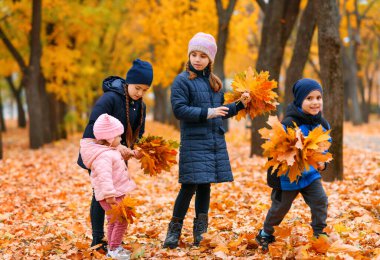 Sonbahar şehir parkında sarı akçaağaç yapraklarıyla oynayan çocuklar. Sonbahar mevsimi, güzel doğa..