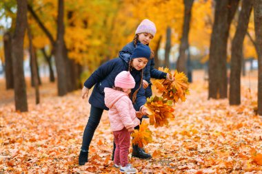 Autumn City Park 'ta oynayan kızlar. İki çocuk sarı akçaağaç yapraklarıyla oynuyor. Sonbahar mevsimi, sarı ağaçlı güzel doğa..
