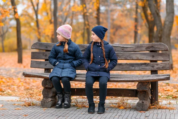 秋の都市公園の子供たちの肖像 幸せな人々が美しい黄色の葉を背景にポーズをとって 木製のベンチに座って — ストック写真