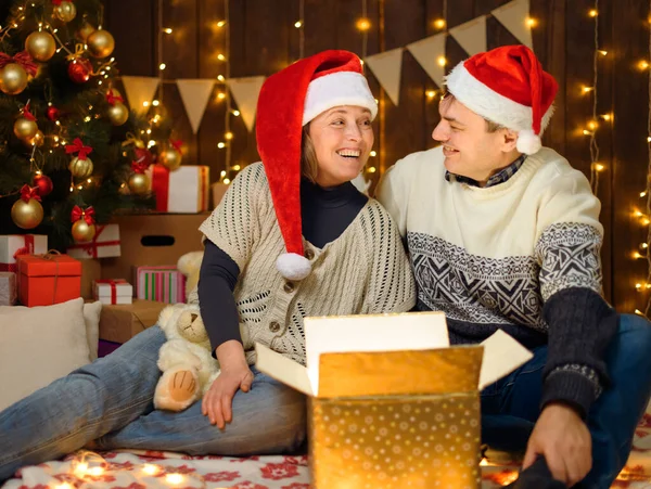 一对夫妇在新年装饰中的肖像 他们打开一个盒子 玩得很开心 节日彩灯 礼物和装饰有玩具的圣诞树 — 图库照片