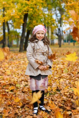 Sarı yapraklarla oynayan kız. Sonbahar parkındaki mutlu bir çocuğun portresi..