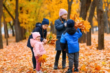 Sonbahar şehir parkında sarı akçaağaç yapraklarıyla oynayan çocuklar. Sonbahar mevsimi, güzel doğa..