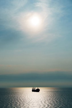 Denizdeki gemi siluetleri, günbatımı gökyüzü ile dramatik deniz manzarası, dalgalardan yansıyan parlak güneş ışığı.