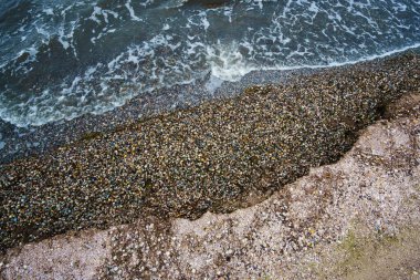 Üst manzara, arka plan olarak dramatik deniz manzarası, kasvetli deniz ve dalgalar, deniz kabuklarıyla dolu kıyı şeridi, sonbaharın sonlarında vahşi manzara, bulutlu hava.