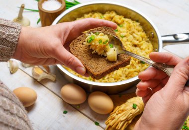 Bir kadının eli kızarmış lahana alır tavada, sarımsak ve yeşil soğan, peynir, çiftlik yumurtası ve tuz, çiğ ve pişmiş gıdalar beyaz ahşap bir arka planda kırsal tarzda