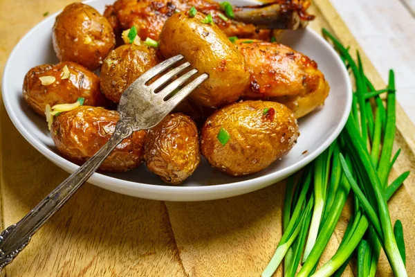 田舎風のおいしいランチ 健康的な食べ物 揚げ鶏の肉と皿の上に皮をむいたローストポテト 緑のネギ ニンニク 白い板の上で調理された食べ物 — ストック写真