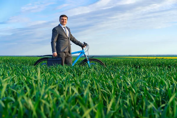 ビジネスコンセプト ビジネスマンは緑の芝生のフィールドに自転車に乗って ビジネススーツを着て 彼はブリーフケースと書類を持っています — ストック写真