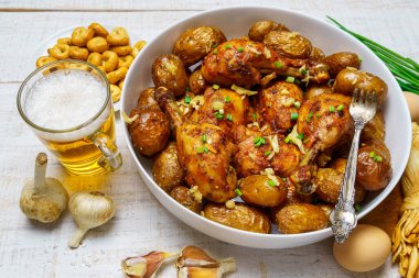 Lezzetli yemek, kırsal tarzda öğle yemeği - bir bardak bira, kızarmış tavuk eti ve patates, sarımsak ve yeşil soğan, peynir, çiftlik yumurtası ve tuz, beyaz ahşap bir tahtanın üzerinde pişmiş yemek