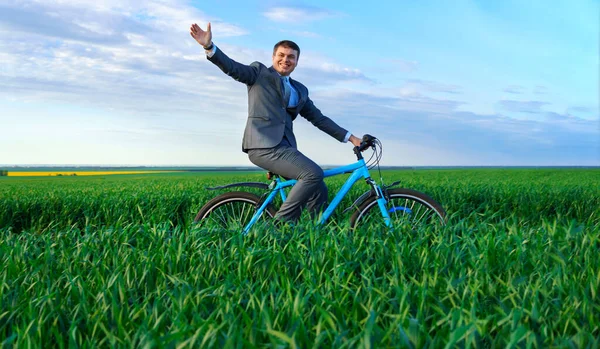 商人骑着自行车穿过绿色的草地 挥挥手 穿着西装 春天的美丽自然 商业观念 — 图库照片