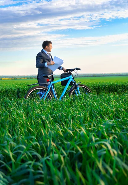 ビジネススーツに身を包んだビジネスマン緑の草原の中で自転車とポーズを取り 文書やレポートを読み取り 春の美しい自然 ビジネスコンセプト — ストック写真
