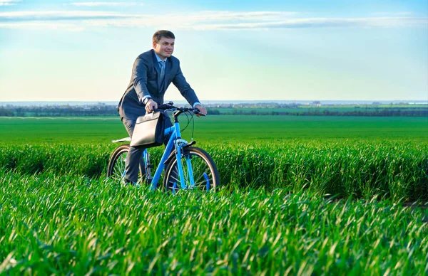 ビジネスマンは緑の草原を自転車で走り ビジネススーツを着て ブリーフケースと書類 春の美しい自然 ビジネスコンセプトを持っています — ストック写真