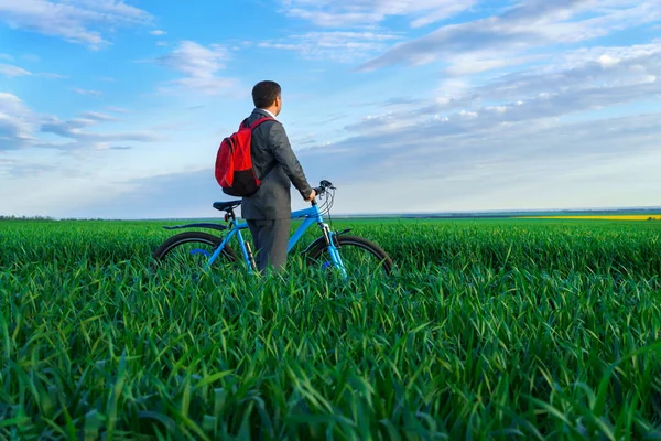 ビジネスマンは遠くを見渡し緑の草原をバックパックと自転車で立ちビジネススーツに身を包み春の美しい自然ビジネスコンセプト — ストック写真