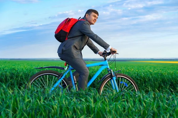 ビジネスマンは緑の草原をバックパックで自転車に乗り春にはビジネススーツに身を包んだ美しい自然ビジネスコンセプト — ストック写真