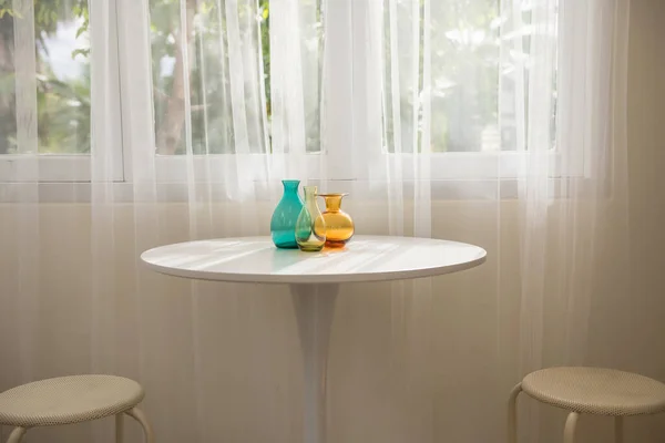 Garrafas Translúcidas Coloridas Mesa Branca Por Janela Cadeiras Com Luz — Fotografia de Stock