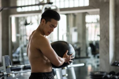 Güçlü Asyalı kaslı adam, spor salonunda karın topunda çıplak vücut egzersizi yapıyor. Spor kulübünde sert top sallayarak egzersiz yapan bir adam. Vücut geliştirme ve sağlıklı yaşam tarzı konsepti.