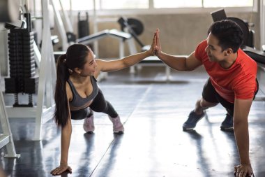 Spor kıyafetleri içinde gülümseyen genç bir çift egzersiz yapıyor ve spor salonunda beşlik çakıyor. Mutlu Asyalı erkek ve kadınlar için spor ve sağlıklı yaşam tarzı.