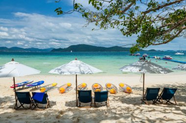 Beach chairs, parasols , surfboard, kayak boat on the white sand beach with cloudy blue sky at Hey island, Phuket, Thailand. Famous travel destination or holiday maker of Siam. Andaman sea of Thai southern.