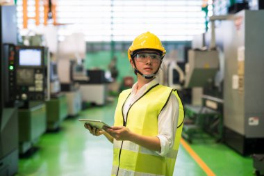 Fabrika atölyesindeki transistör mikroçip makinelerini kontrol etmek için tablet kullanan kalın şapka ve koruma gözlüğü takan Asyalı işçiler. Yüksek teknolojili sanayi üretimi.