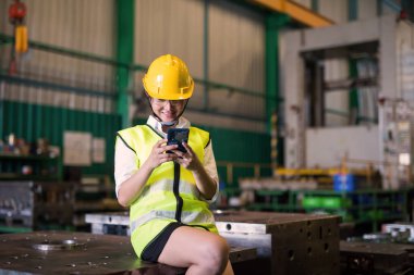 Gülümseyen fabrika kadın çalışanı sosyal medya, sohbet, mesaj, öğlen arasında depo içinde online alışveriş yapmak için akıllı telefon kullanıyor. Kadınlar çok çalıştıktan sonra rahatlar..