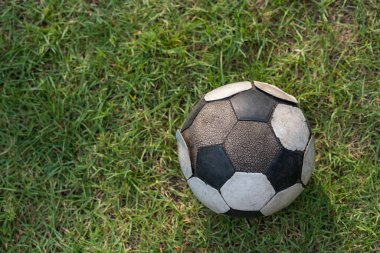 Yeşil çimlerin üzerinde eski bir futbol topu. Üstten bakınca doğal ışık ve gölgeli. Grunge futbol derisini kötü durumda kırmış..
