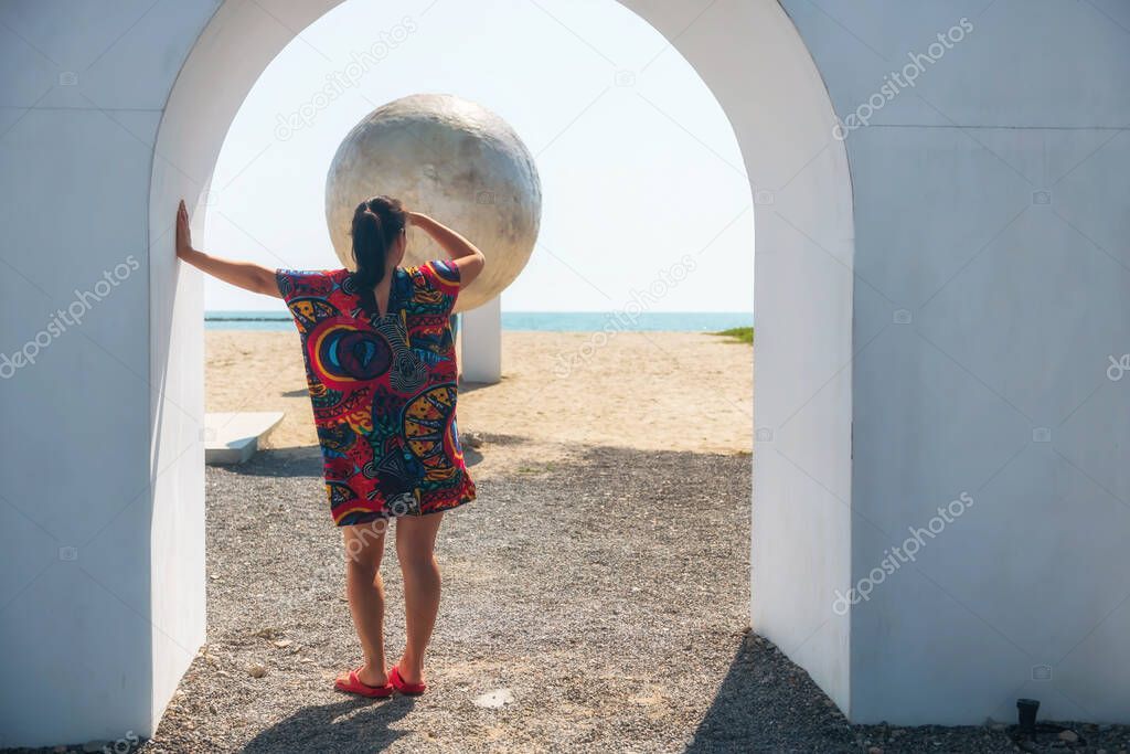 Rear of Asian woman in Hawaii dress look at fake moon on beach, Cha-Am, Phetchaburi. Holiday maker or summer vacation in tropical country, Thailand or Siam.